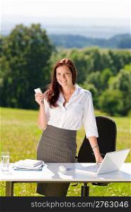 Young businesswoman in sunny nature office calling standing behind table