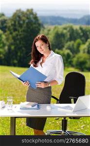 Young businesswoman in sunny nature office holding folder behind table