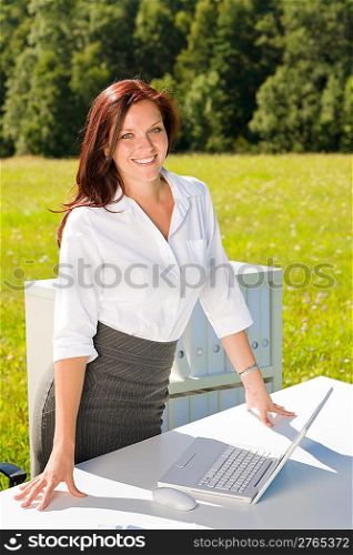 Young businesswoman in sunny nature office smiling standing behind table