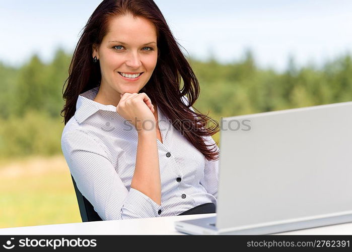 Young businesswoman in sunny nature with laptop behind table smiling