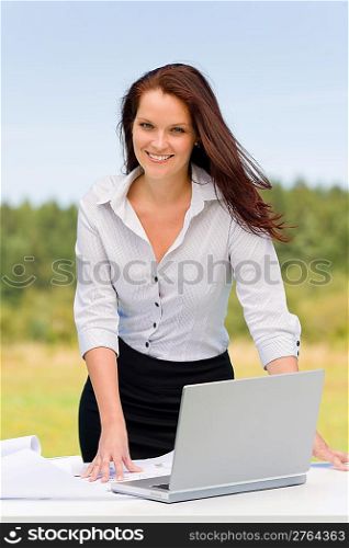 Young businesswoman in sunny nature with laptop behind table smiling