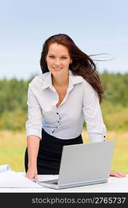 Young businesswoman in sunny nature with laptop behind table smiling