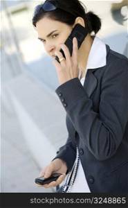 Young businesswoman is using two mobile phones at the some time. She is outdoor, somewhere in the downtow district.