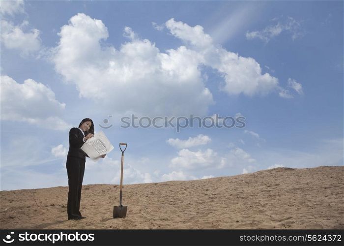 Young businesswoman looking at a blueprint next to a shovel in the middle of the desert