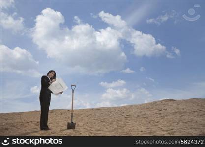 Young businesswoman looking at a blueprint next to a shovel in the middle of the desert