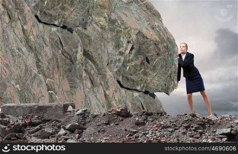 Young businesswoman making effort to move huge stone
