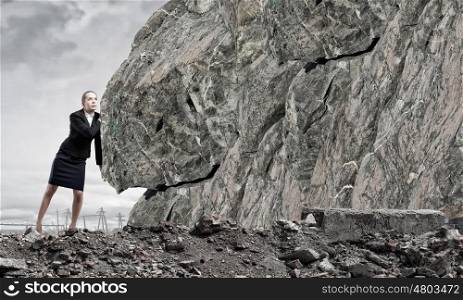 Young businesswoman making effort to move huge stone