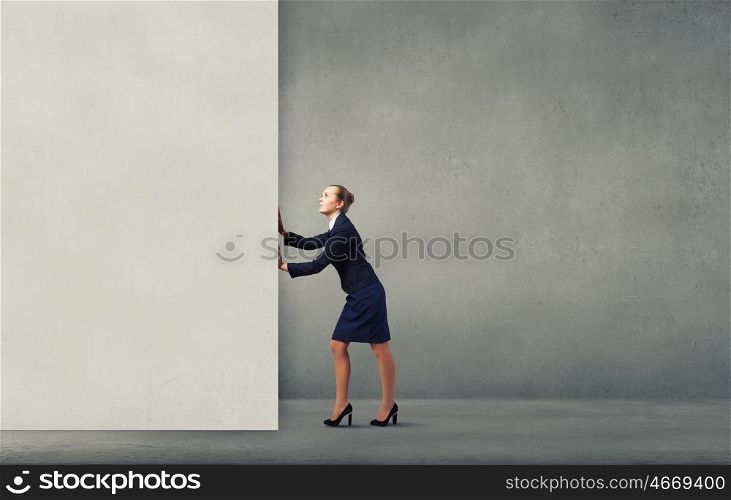 Young businesswoman making effort to move wall. Strong enough