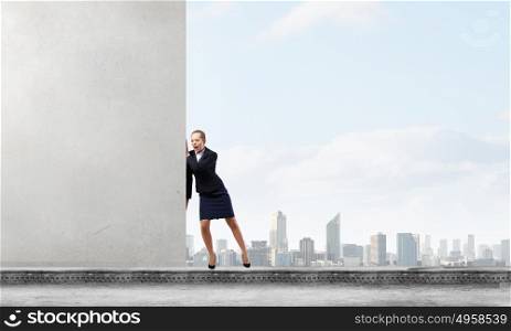 Young businesswoman making effort to move wall. Strong enough