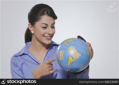 Young businesswoman pointing at globe against gray background