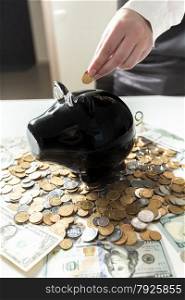 Young businesswoman putting coin in black piggy bank