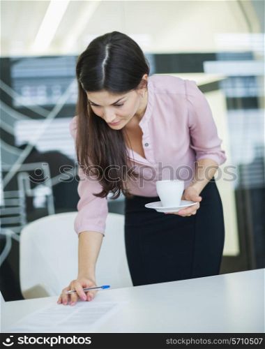 Young businesswoman reading document while holding coffee in office