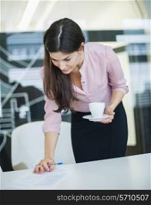 Young businesswoman reading document while holding coffee in office