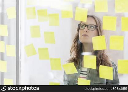 Young businesswoman reading reminders stuck on glass wall