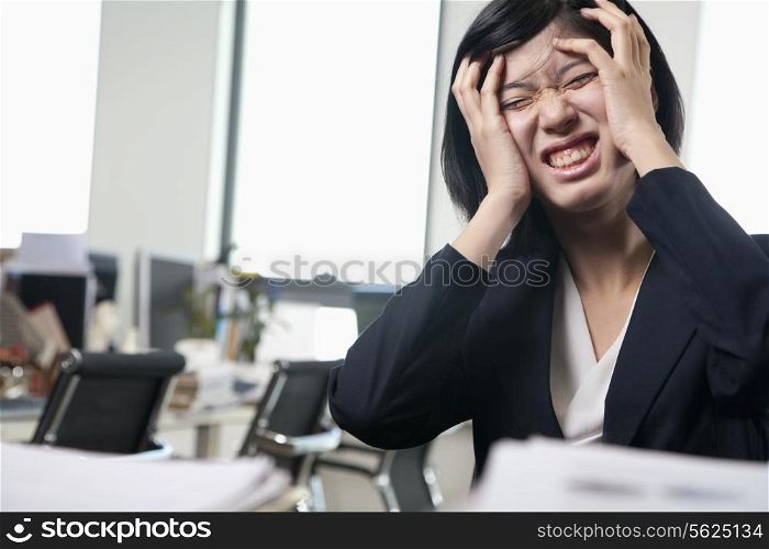 Young businesswoman sitting at desk with head in hands