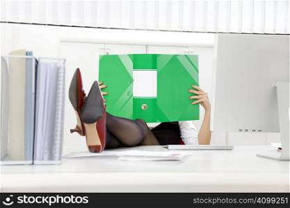 Young businesswoman sitting at desk with legs up and looking at folder