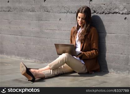 Young businesswoman sitting on floor looking at her laptop computer. Beautiful woman wearing formal wear using earphones.