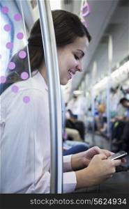 Young businesswoman sitting on the subway and using her phone