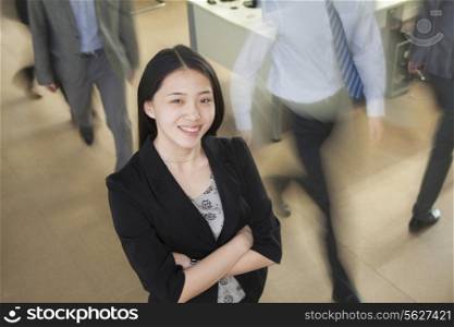 Young businesswoman smiling in the office, businessmen walking all around her