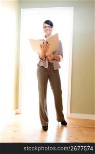 Young businesswoman standing in light-filled doorway and looking at file folder