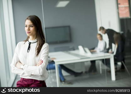 Young businesswoman standing in modern office with young business people in the background who shaking hands