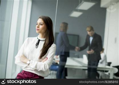 Young businesswoman standing in modern office with young business people in the background who sitting