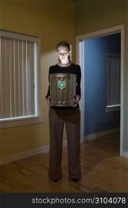 Young businesswoman standing in office, holding and looking into an illuminated trash or recycling bin