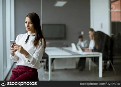 Young businesswoman standing in the office and  using mobile phone