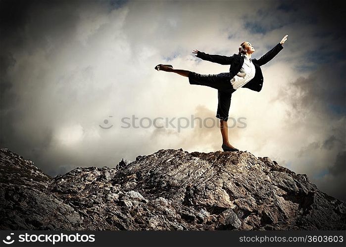 young businesswoman standing on one leg atop of mountain against diagram background