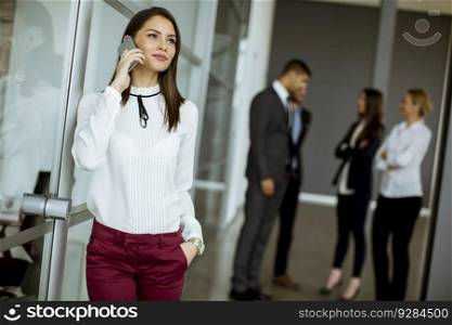 Young businesswoman talking on mobile phone in the office while other business people talking in the background