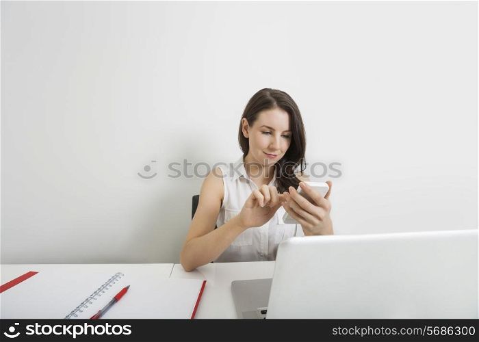 Young businesswoman text messaging through cell phone at desk in office