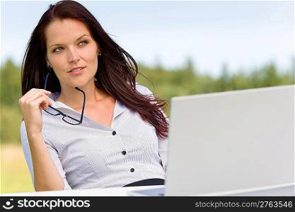 Young businesswoman thoughtful sunny nature with laptop behind table