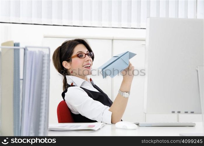 Young businesswoman throwing paper airplane in office