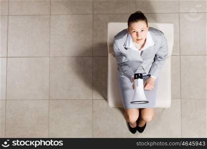 Young businesswoman. Top view of businesswoman sitting on chair with megaphone in hand