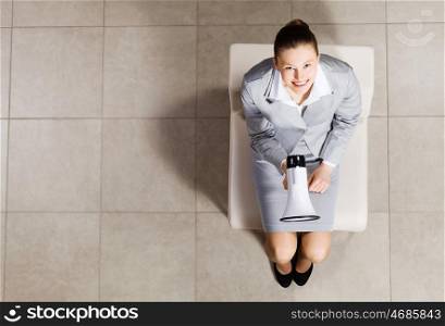 Young businesswoman. Top view of businesswoman sitting on chair with megaphone in hand