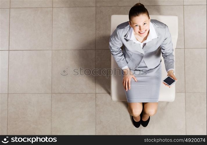 Young businesswoman. Top view of businesswoman sitting on chair with mobilephone in hand