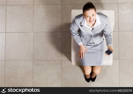 Young businesswoman. Top view of businesswoman sitting on chair with mobilephone in hand