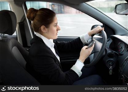 Young businesswoman typing message while driving a car