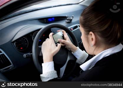 Young businesswoman typing text on smartphone at car