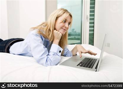 Young businesswoman using laptop while lying in bed