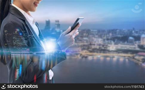 Young businesswoman using mobile phone with modern city buildings background. Future telecommunication technology and internet of things ( IOT ) concept.. Internet of things - Telecommunication Technology