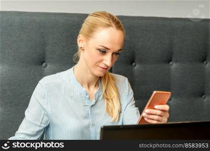 Young businesswoman using smartphone sitting at the table with laptop in cafe. Businesswoman using smartphone in cafe