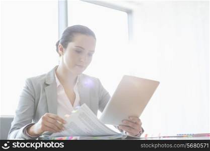 Young businesswoman using tablet PC while reading book in office