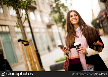 Young businesswoman walking down the street with coffee and cell phone in hand