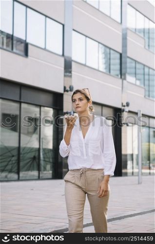 young businesswoman walking near office building talking mobile phone
