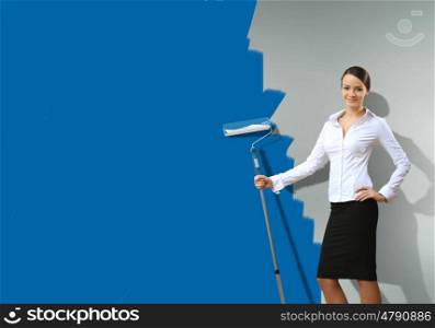 Young businesswoman with a paint brush against blue wall