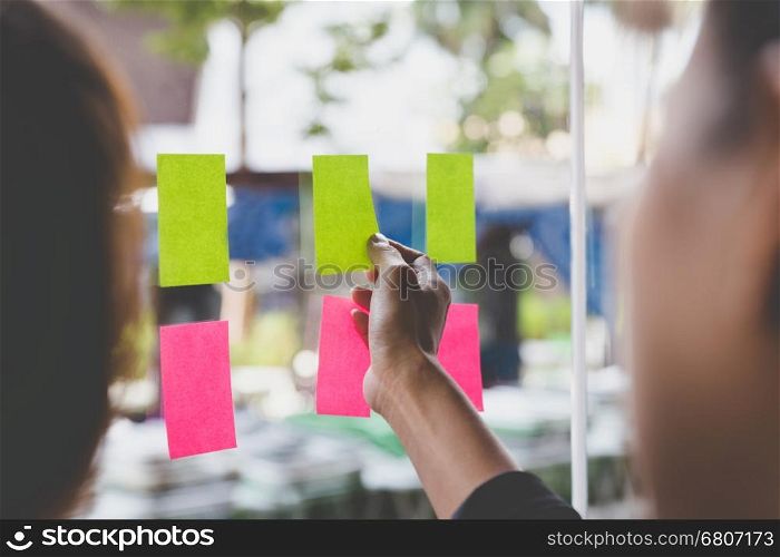 young businesswoman with colleague sticking adhesive notes on window in office