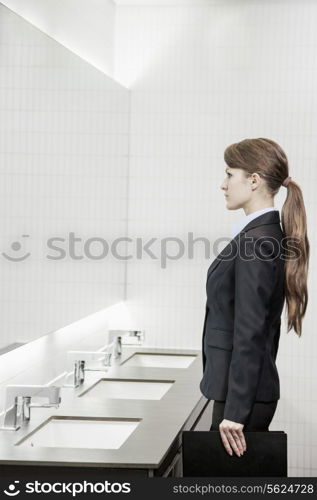 Young businesswoman with long hair looking into the mirror and preparing herself in the bathroom