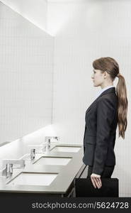 Young businesswoman with long hair looking into the mirror and preparing herself in the bathroom