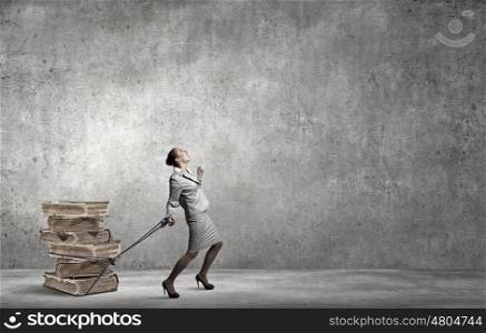Young businesswoman with ropes on hands pulling pile of books. With tied hands